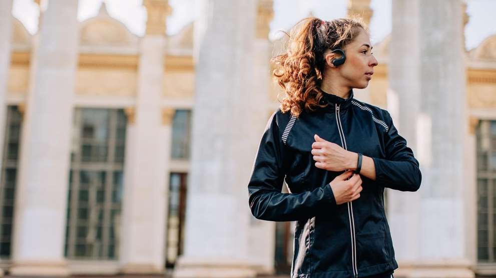 Portrait of young female athlete wearing sport jacket listening portable music player outdoors during the training session in the morning